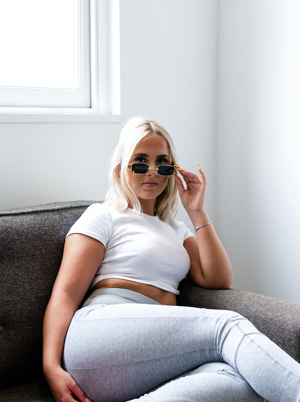 Woman with blonde hair wearing black and gold rectangular retro style shades, in the style BILLIE RETRO.